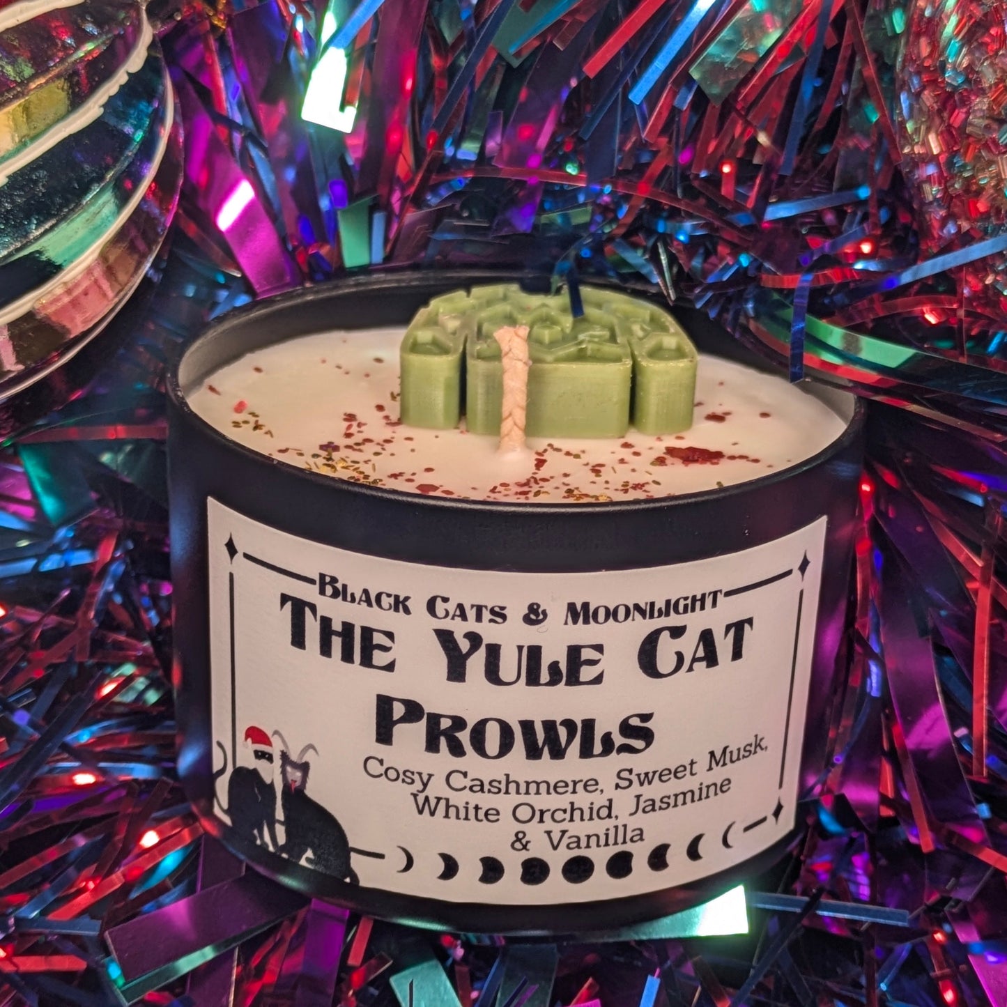 Candle labeled 'The Yule Cat Prowls' on a festive background with tinsel