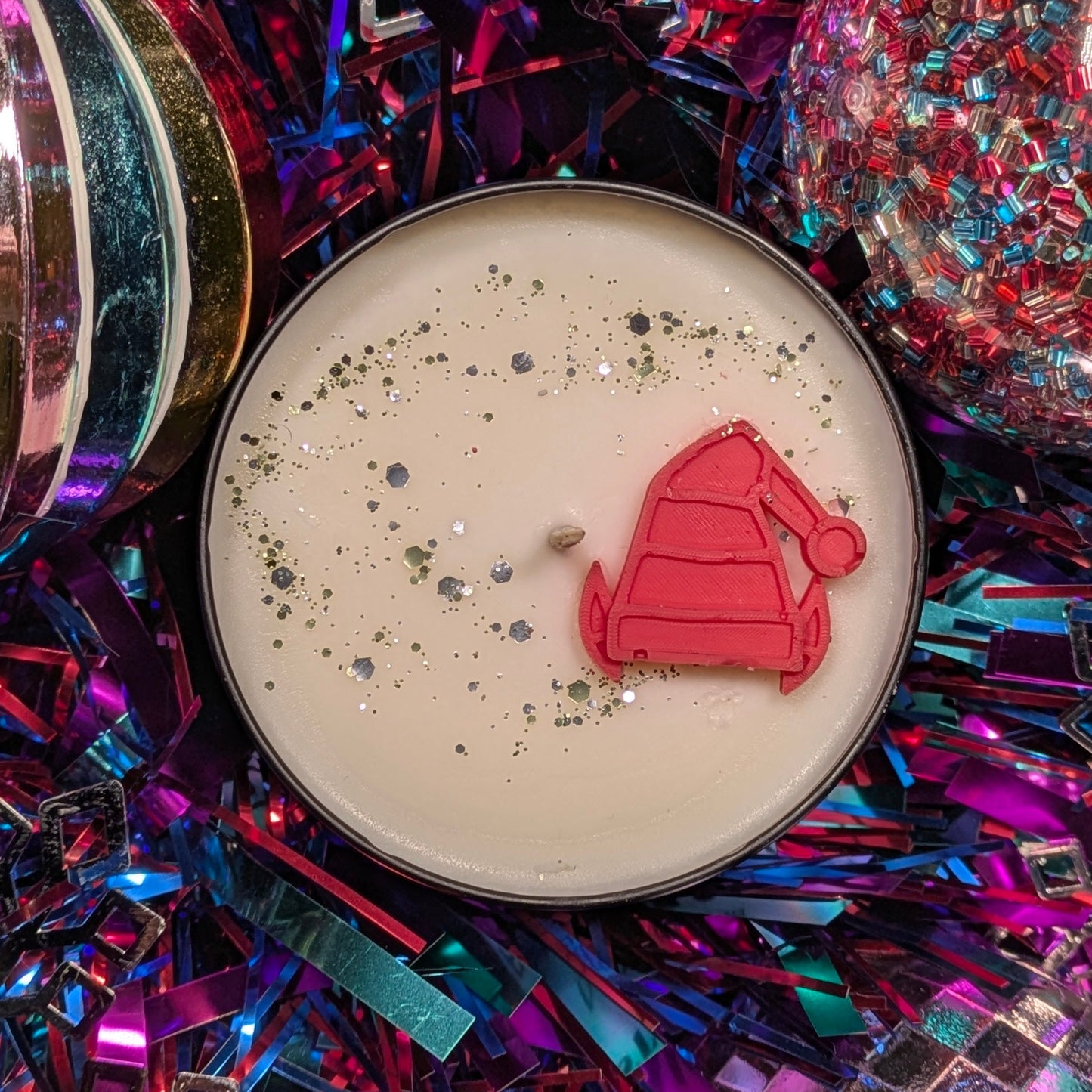 Candle with an elf hat decoration on a colorful, glittery background