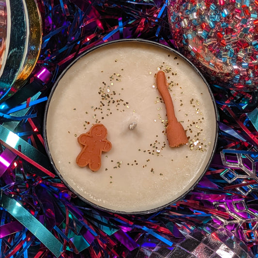 Candle with a gingerbread man and witches broom on top surrounded by festive tinsel