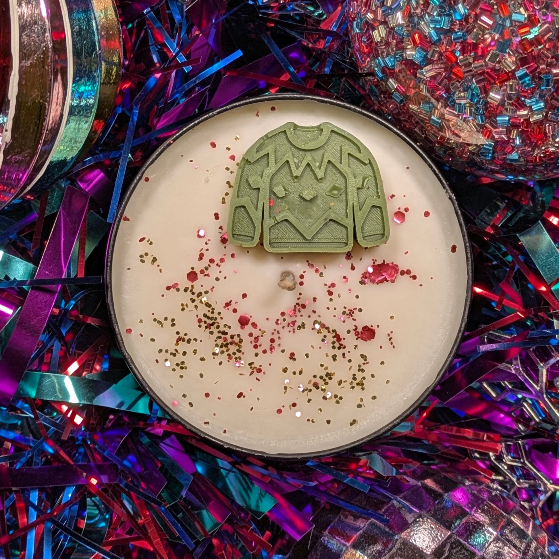 Candle with a green jumper-shaped decoration on a colorful, festive background