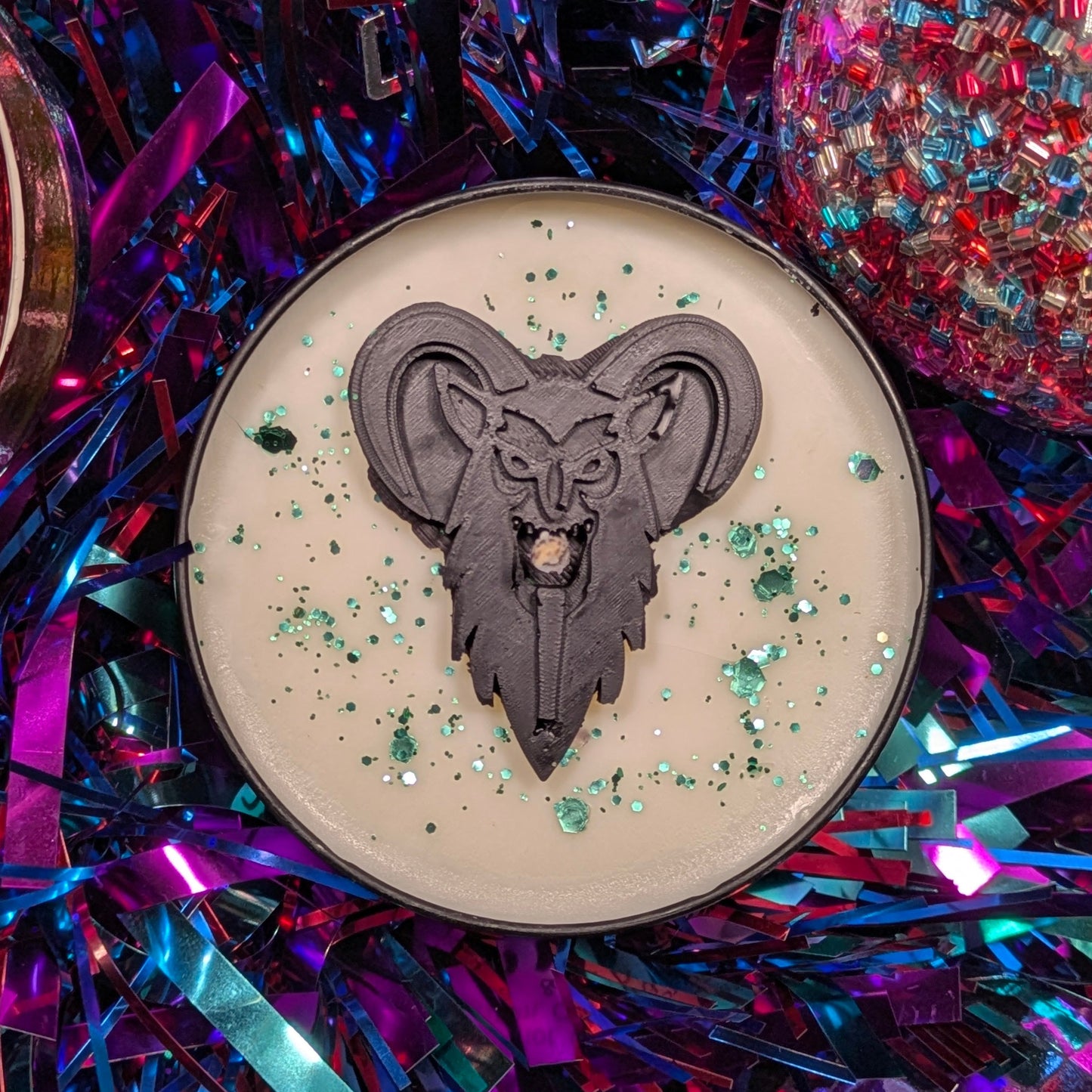 A candle with a krampus head decoration surrounded by festive tinsel
