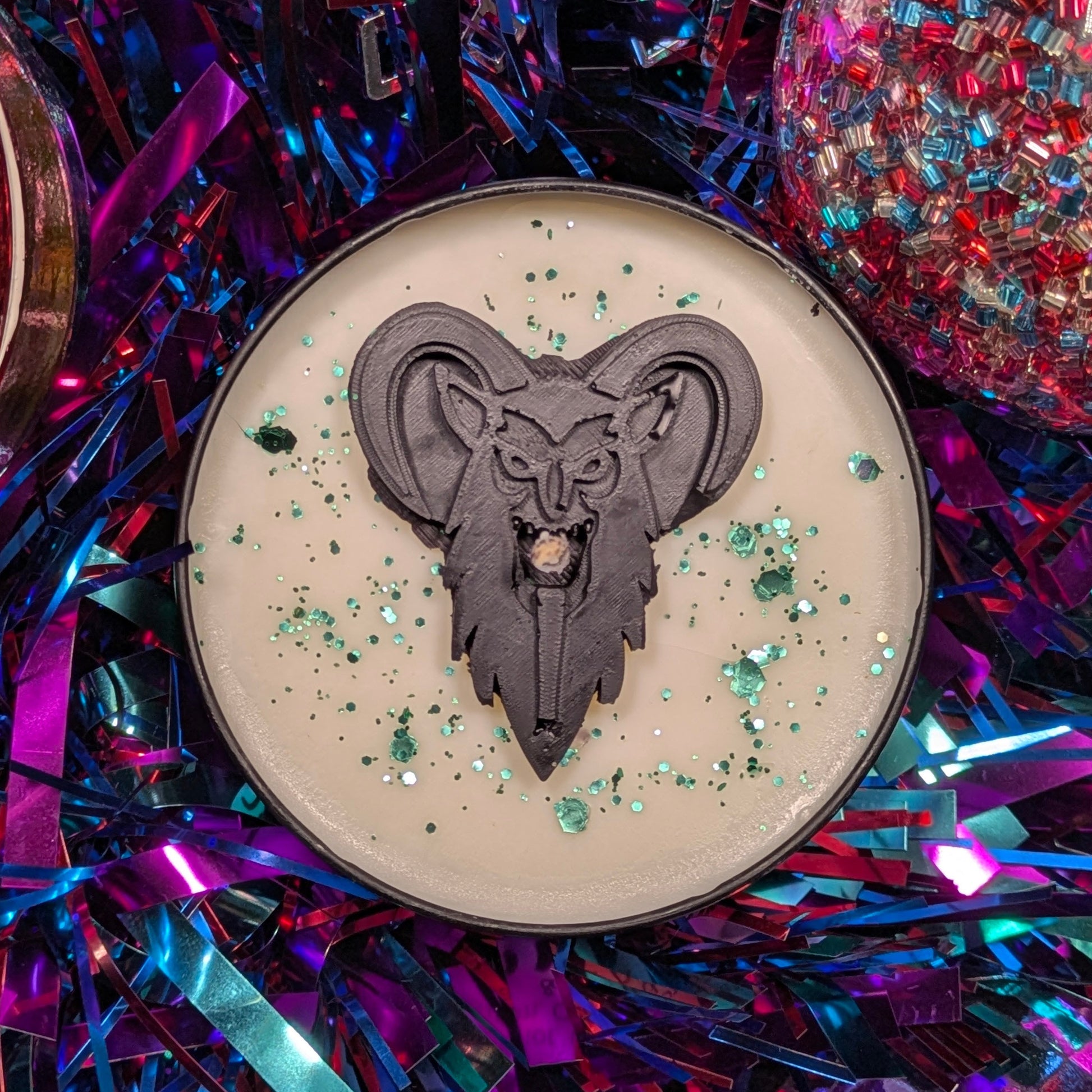 A candle with a krampus head decoration surrounded by festive tinsel